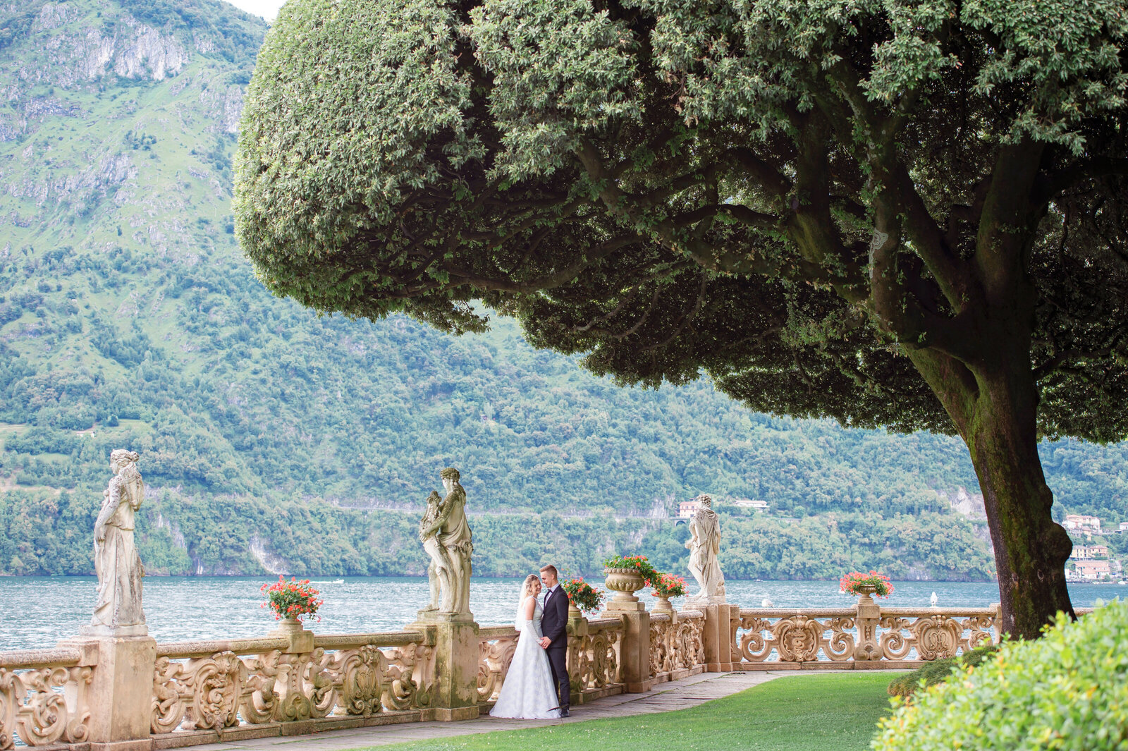 Bride and groom leaning against stone railing by lake