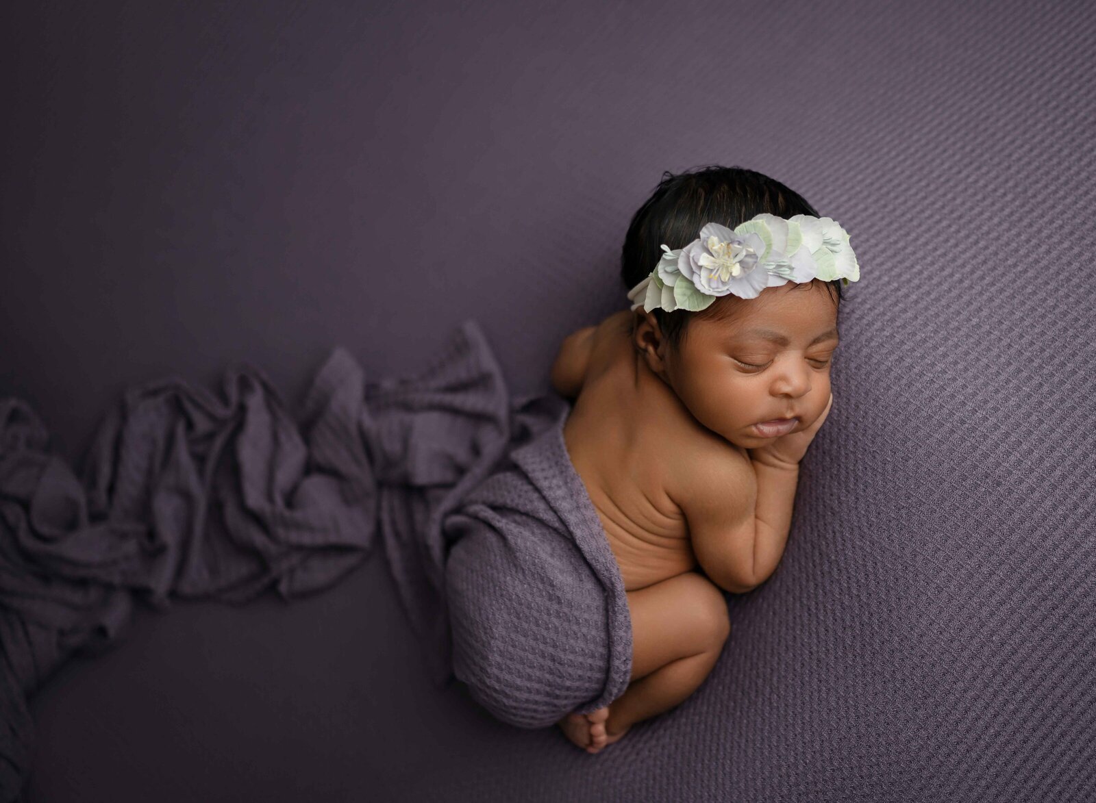 Newborn baby girl sleeping on her tummy with her bum covered up in a purple swaddle.