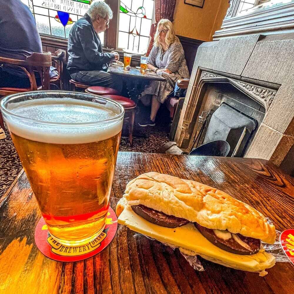 A pint pf real ale with a cheese cob sandwich placed next to it on a wooden table.