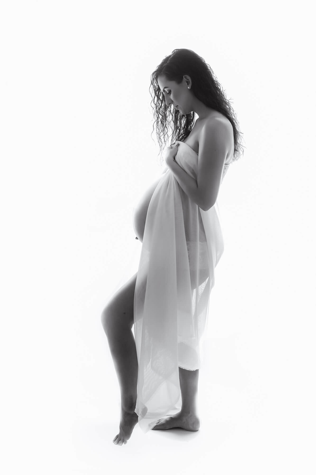 High-key maternity portrait of a pregnant woman draped in white fabric