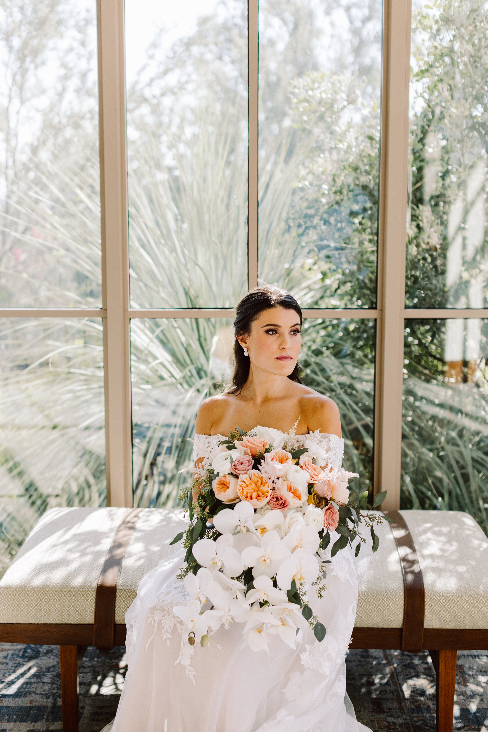 A bride sitting on a bench with a large bouquet of flowers in her hands.