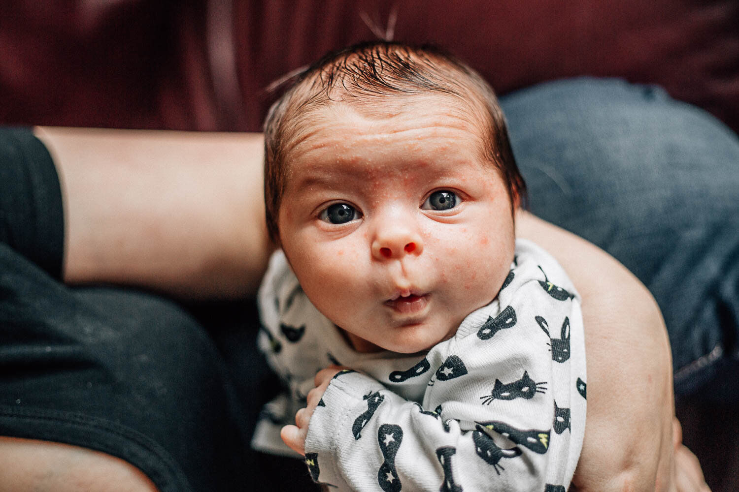 Hampton Roads newborn photographers capture small baby with dark hair awake and looking at the camera with wide eyes as his mother holds him in her arms