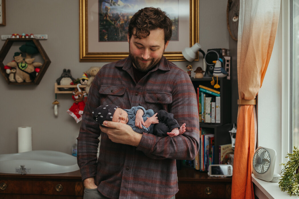 Father holding newborn son during in home lifestyle newborn session with Lux Marina Photography Eugene, Oregon based newborn photographer