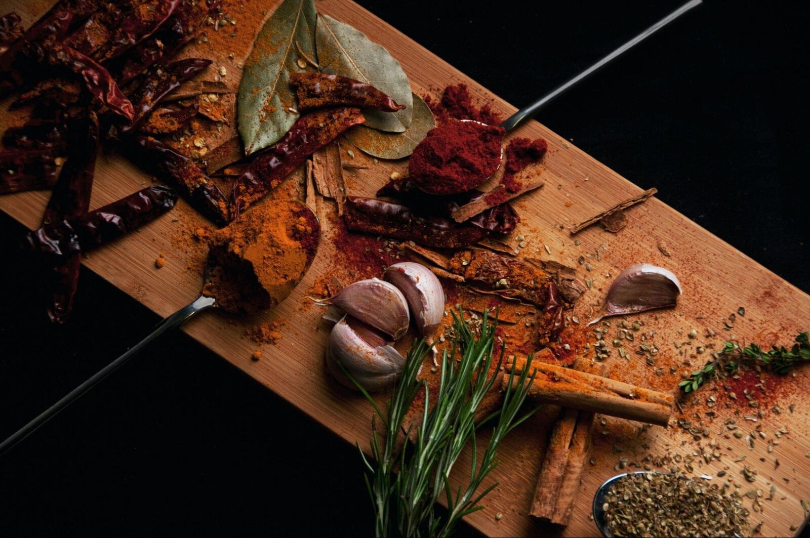 Image: cinnamon sticks, cloves, and various other spices on a brown wooden board