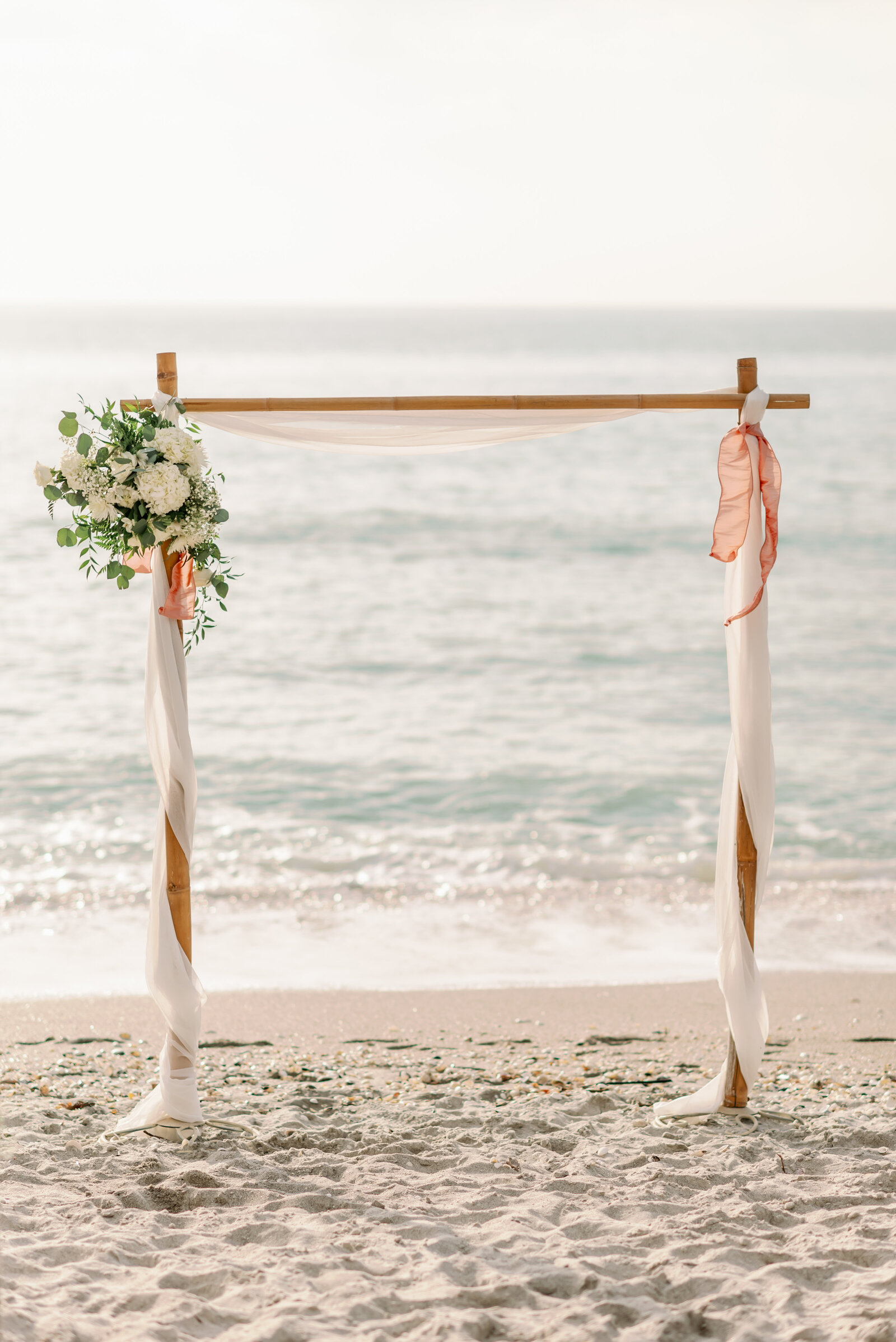Bamboo arch with tulle wrapped around it and a floral arrangement on the top left corner on Captiva Beach, FL