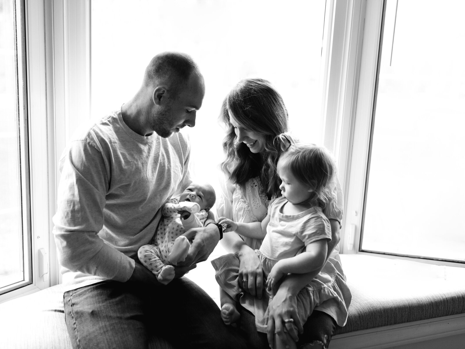 family sitting by window for newborn photoshoot