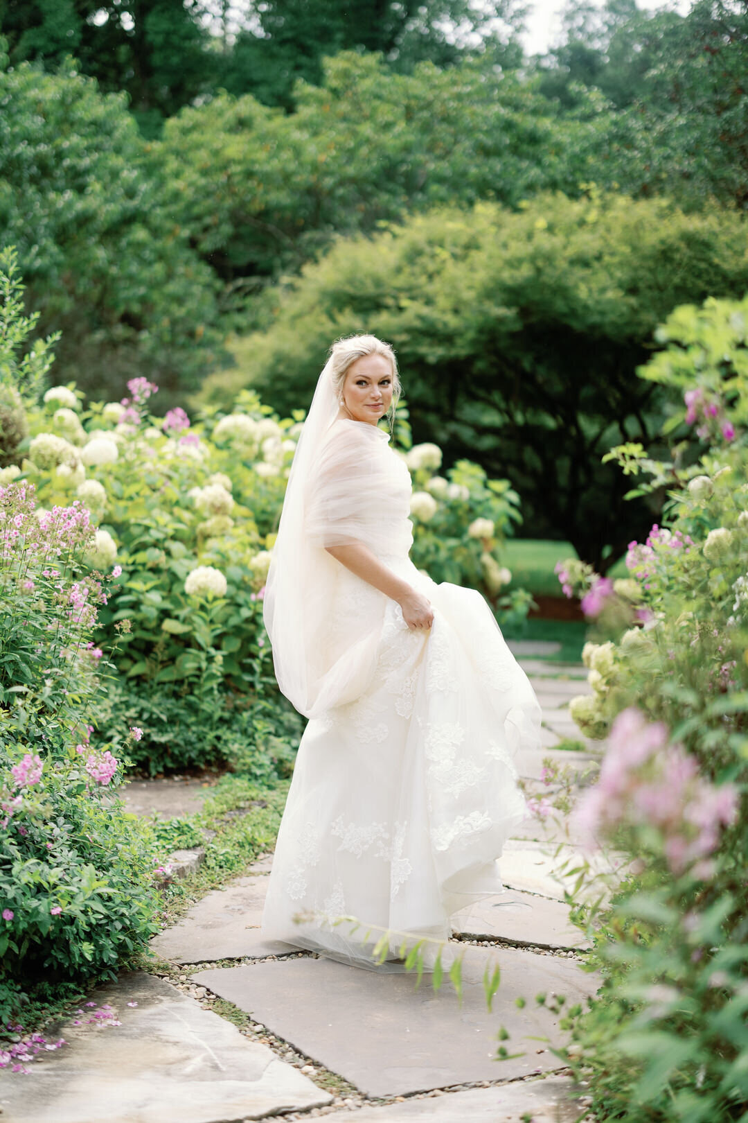 Bride holding train of her dress walking through garden at The Farm at Old Edwards