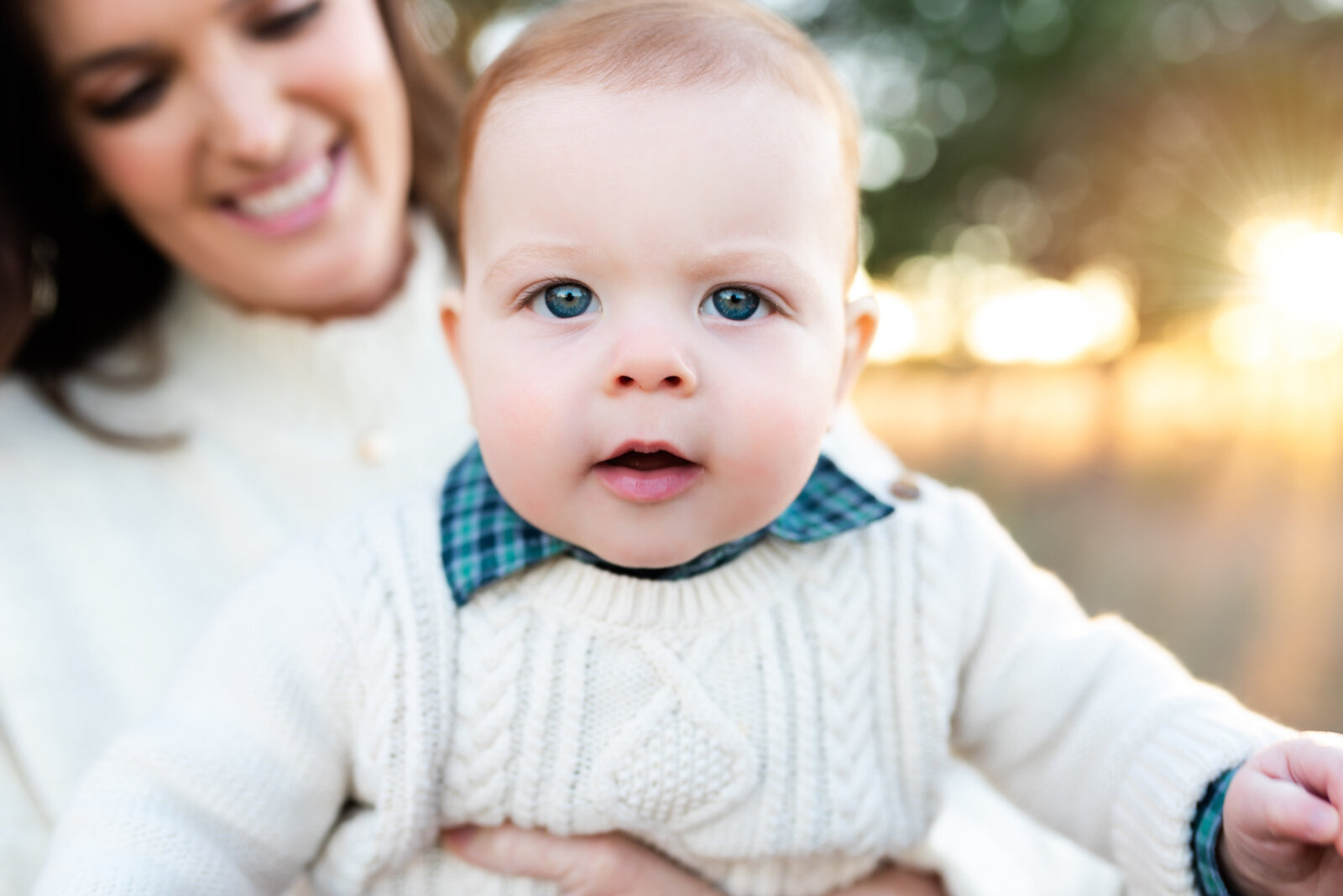Baby boy in a cozy cream sweater smiling at the camera during an outdoor portrait session in Allen, Texas, photographed by Jennifer L. Kirk Photography.