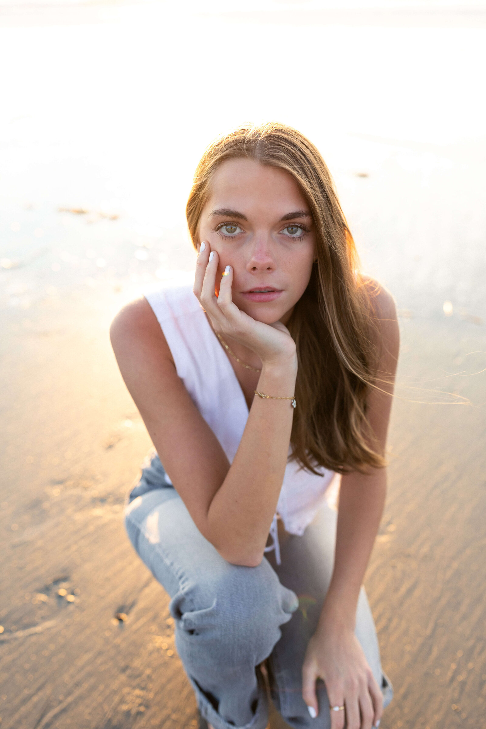 brunette high schooler posing on a beach wearing a white shirt and blue jeans on a sandy beach