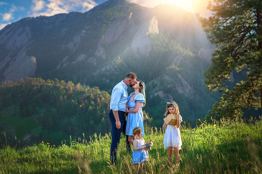 mom-dad-kissing-at-sunset-2-girls-playing-in-field-meadow-mountain-view-hill-top-green-grass-wildflower-NCAR-best-boulder-family-photographer