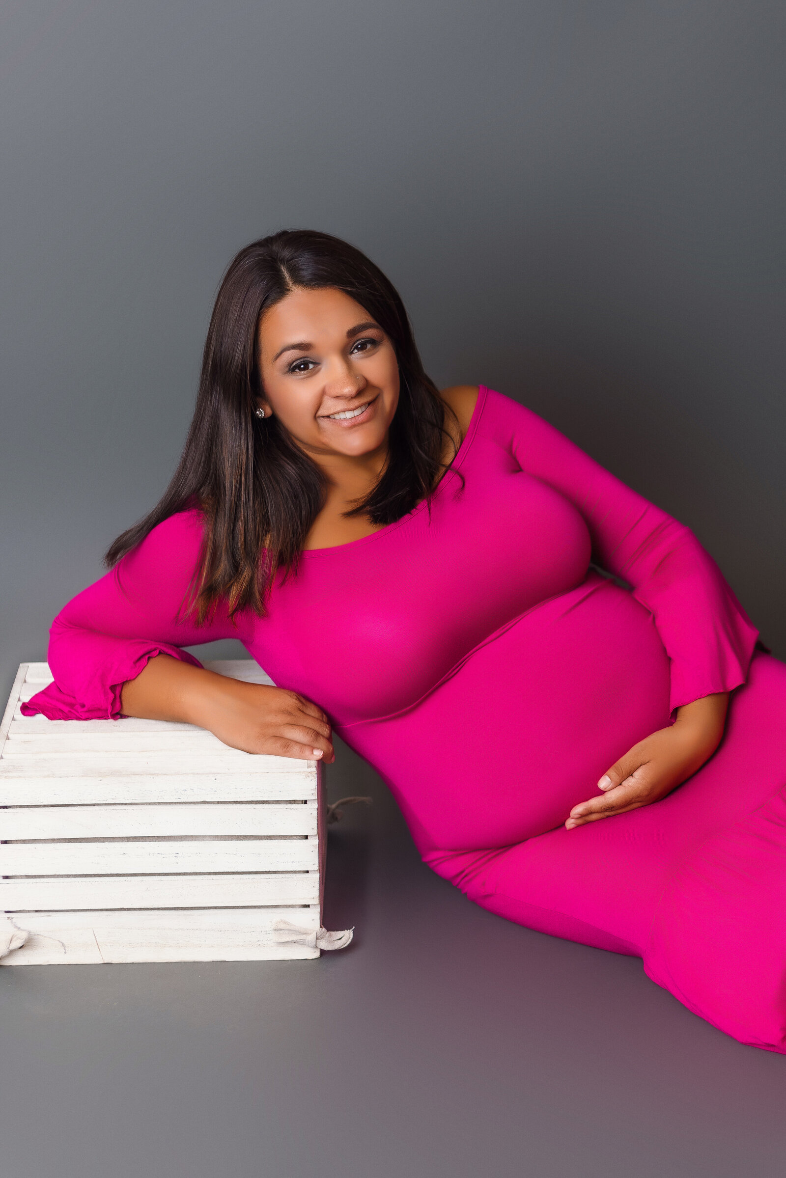 Maternity Photographer, a pregnant mother reclines on a milk crate in a pink gown
