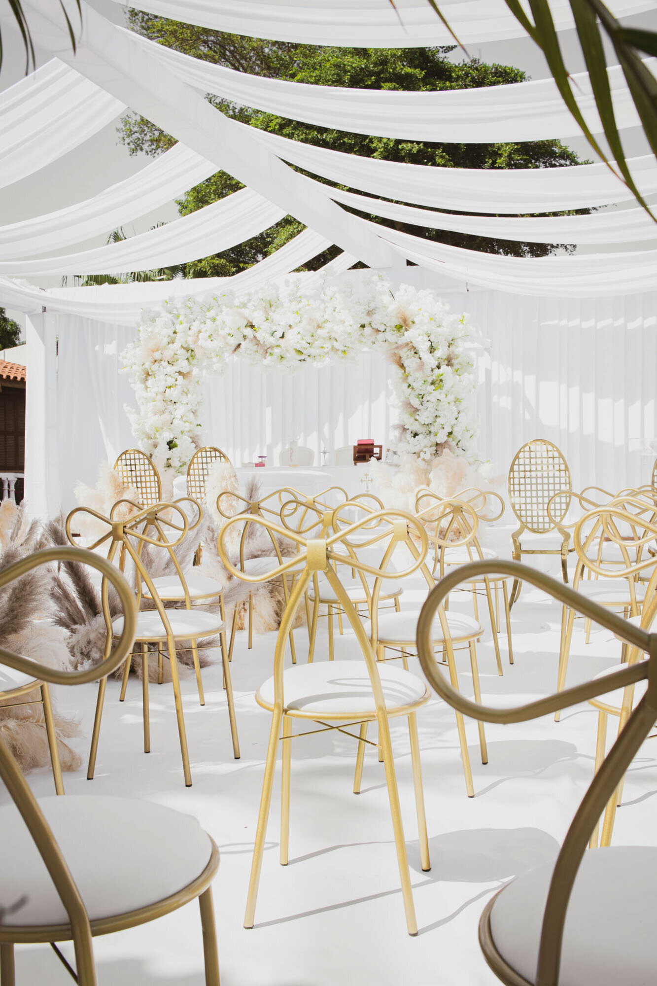 White and gold wedding ceremony setup with bow-back chairs and floral arch