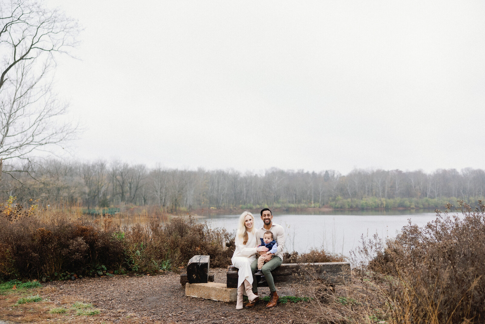 family smiling for family photos at the camera in front of pond at 100 acre woods in indianapolis