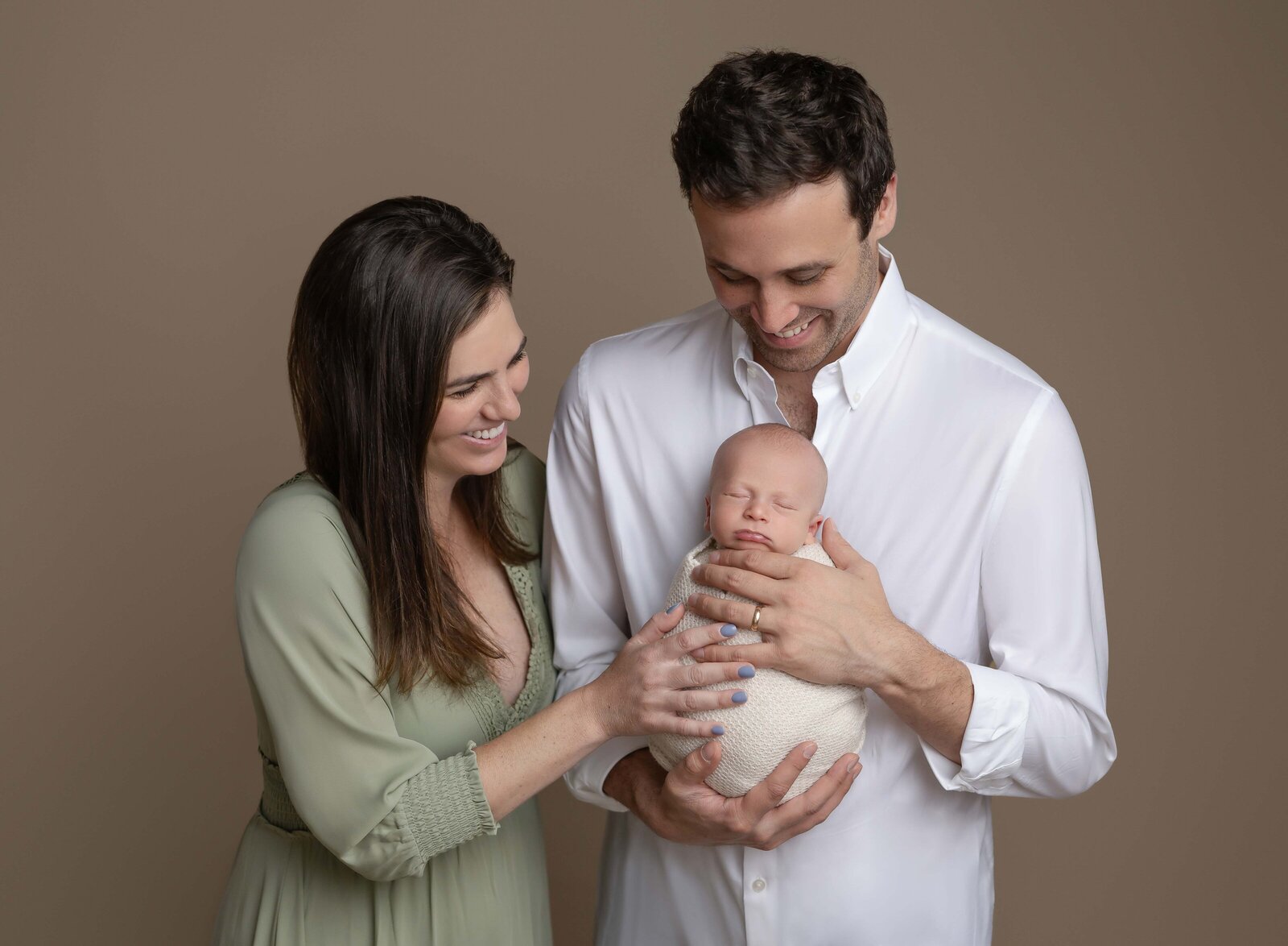 Mom and dad holding newborn and smiling. Photo taken at Marietta Newborn photo studio.