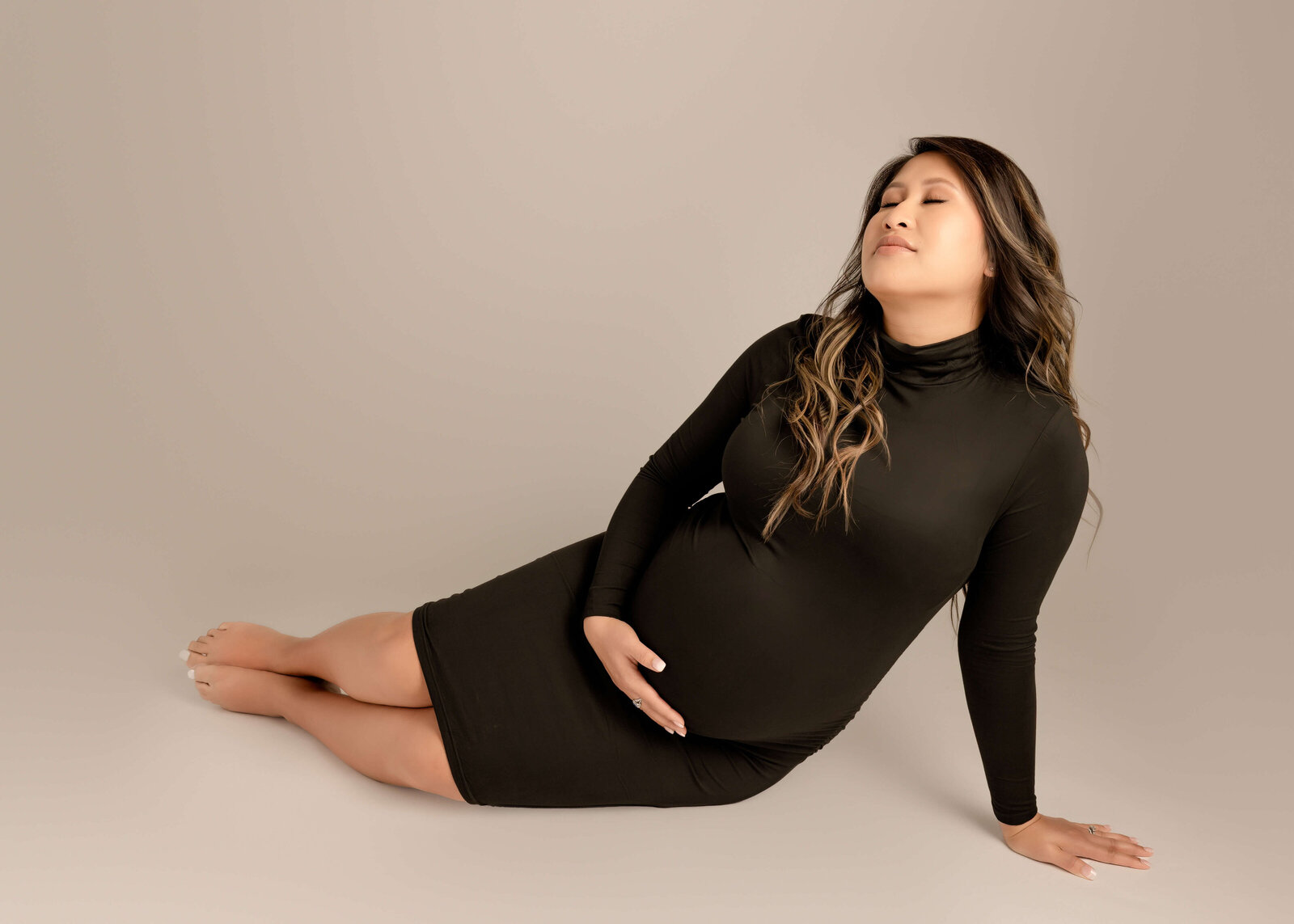Expectant mom in studio maternity session sitting on floor looking up dreaming about her baby in Orange County, CA by Ashley Nicole.