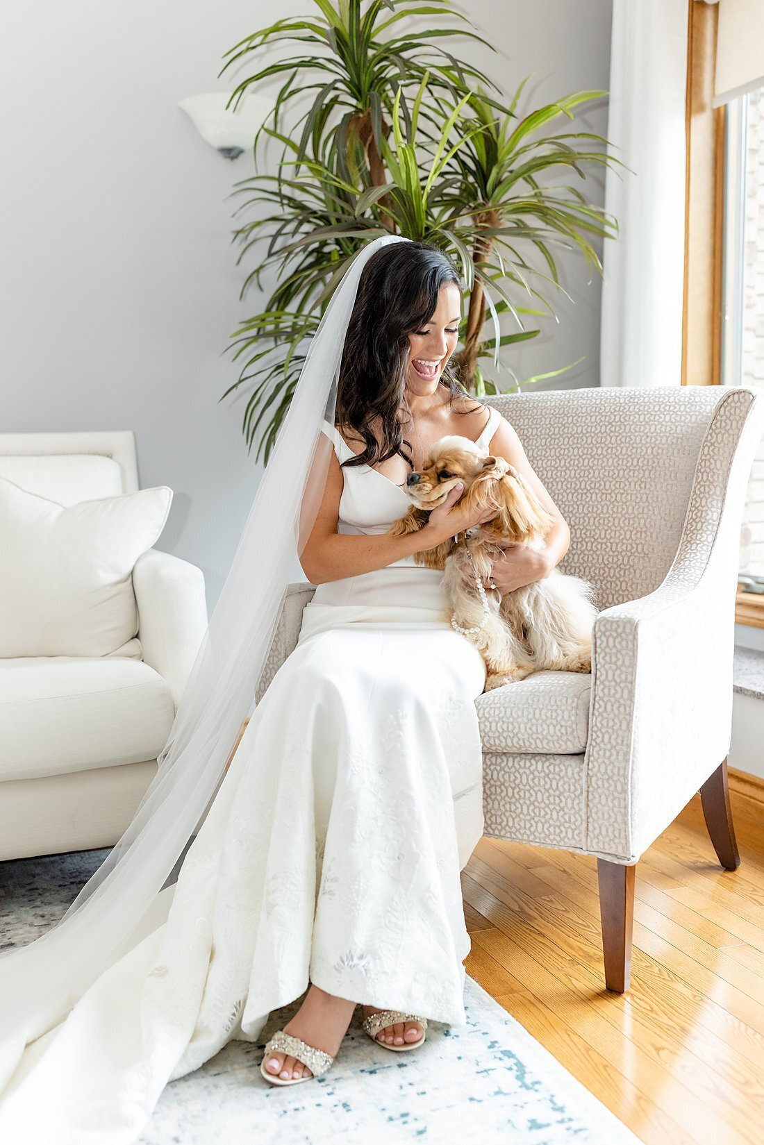 Bride-laughing-and-smiling-as-she-sits-on-a-chair-with-her-little-dog-on-her-lap