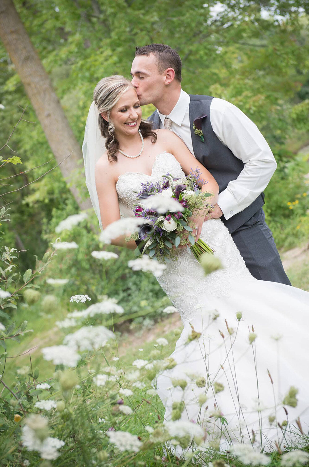groom kisses brides cheek in front of lacey flowers