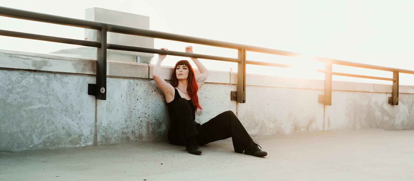 Desiree Electric Honey Photographer Sitting Against Rooftop Railing at Sunset