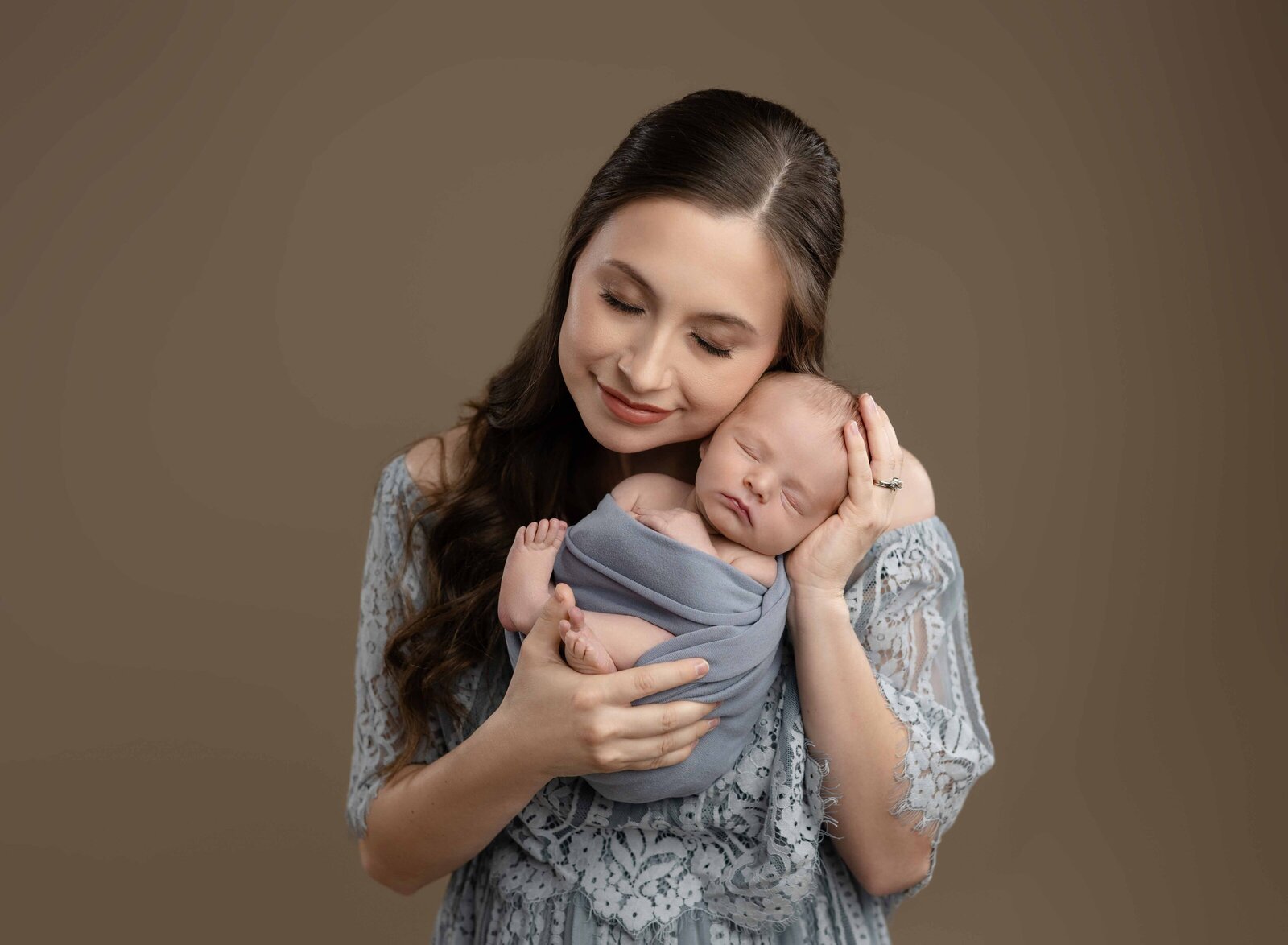 Mom snuggling newborn baby boy who is wrapped in blue cloth.