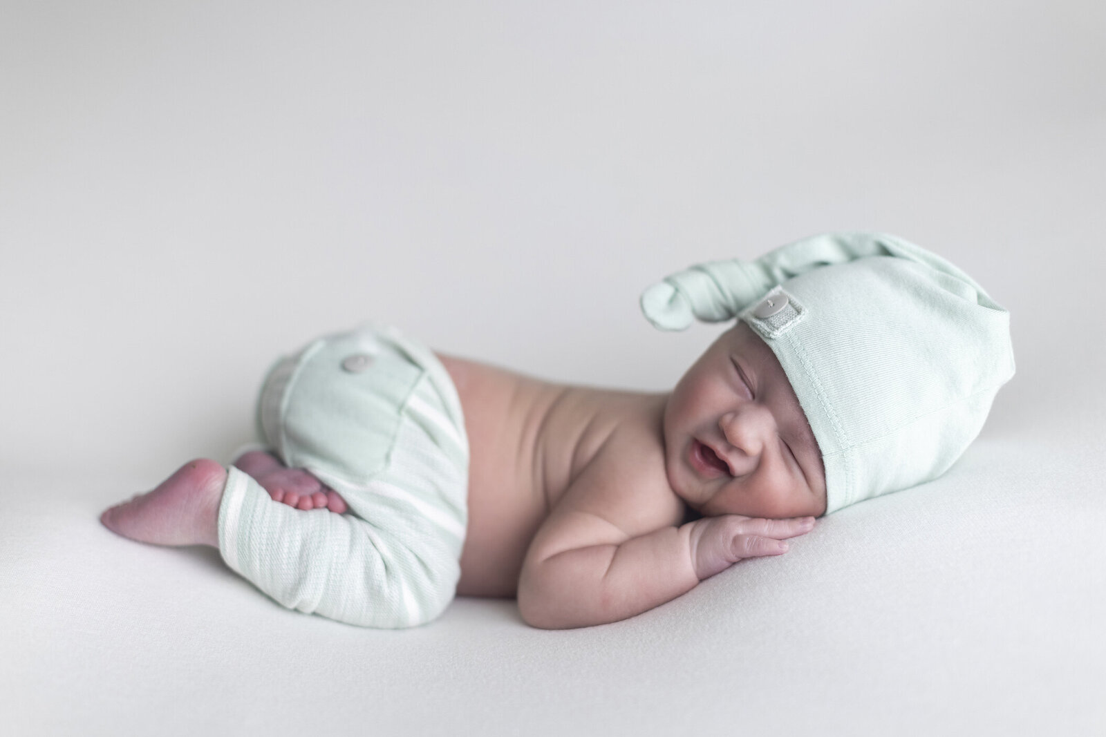 Newborn boy grins on white fabric.