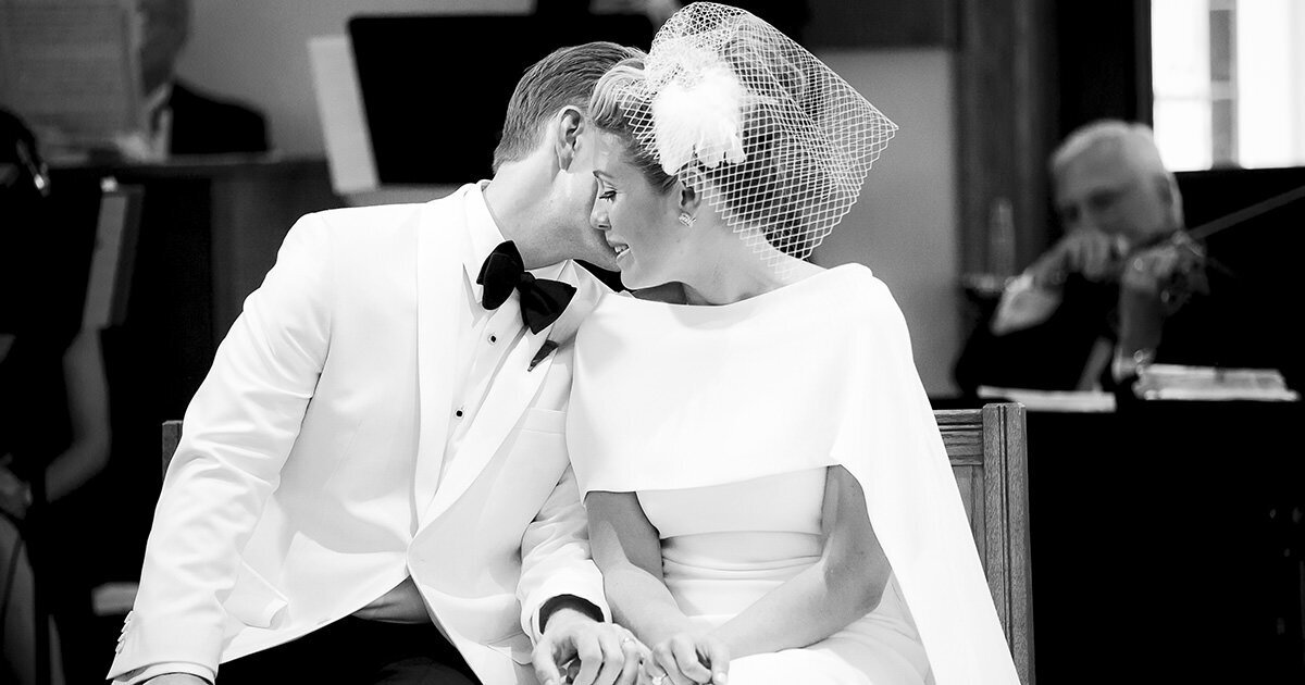 black and white photo of groom whispering to his bride during their wedding ceremony