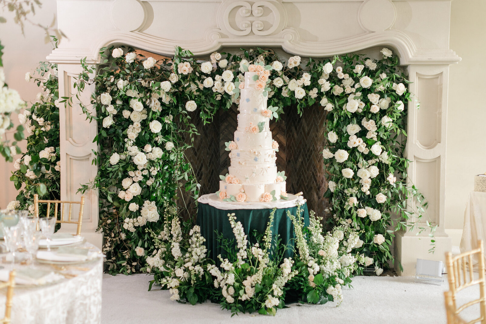 Seven tiered wedding cake made by Carlos Bakery surrounded by an english garden inspired floral wall and arrangements by Sweet Root Village.