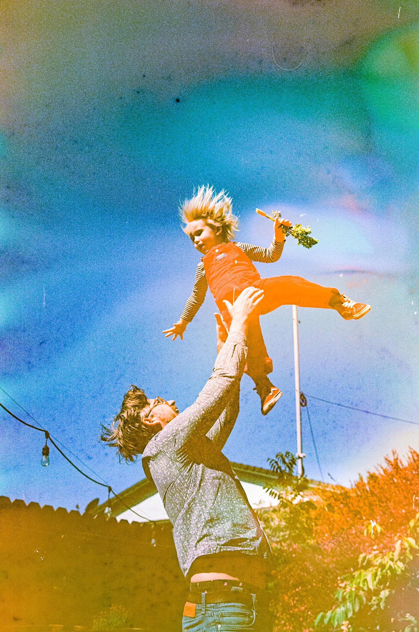 dad throwing young son wearing red overalls up in the air in their backyard