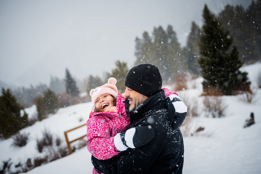 a dad and his daughter stick their tongue out to catch some snow flakes on their tongue