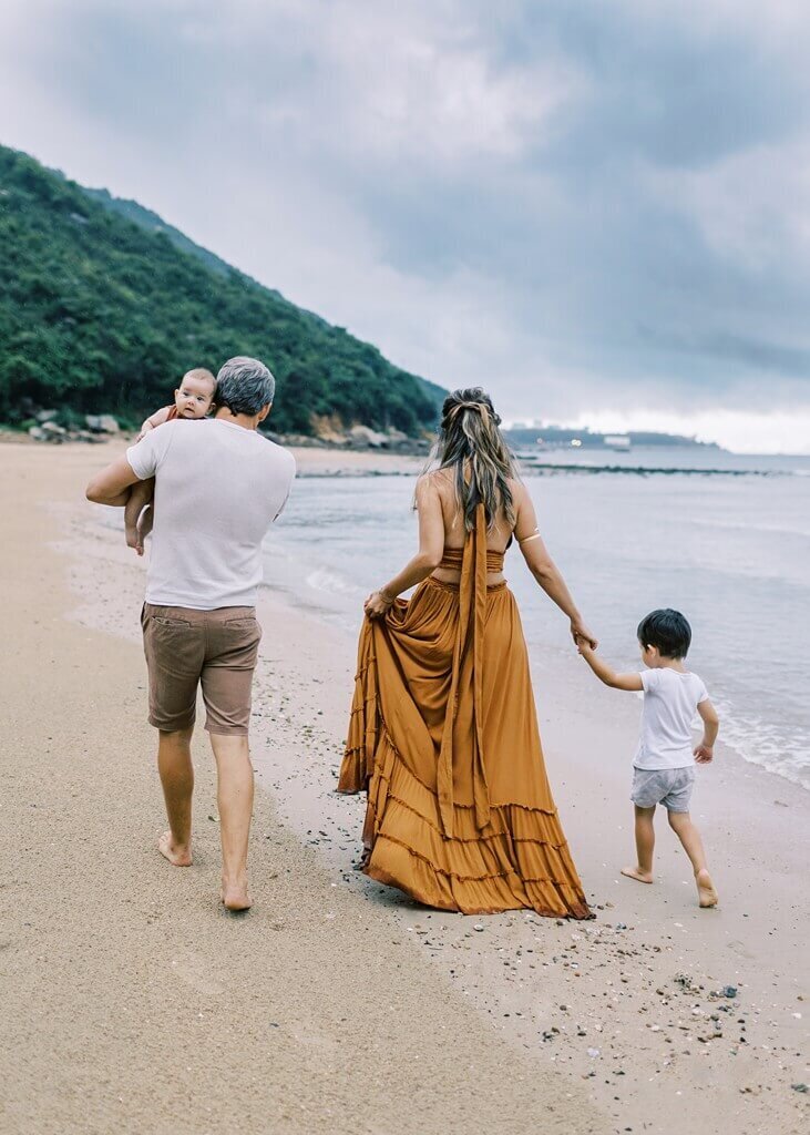 Family of four walking and holding hands at a serene beach location.
