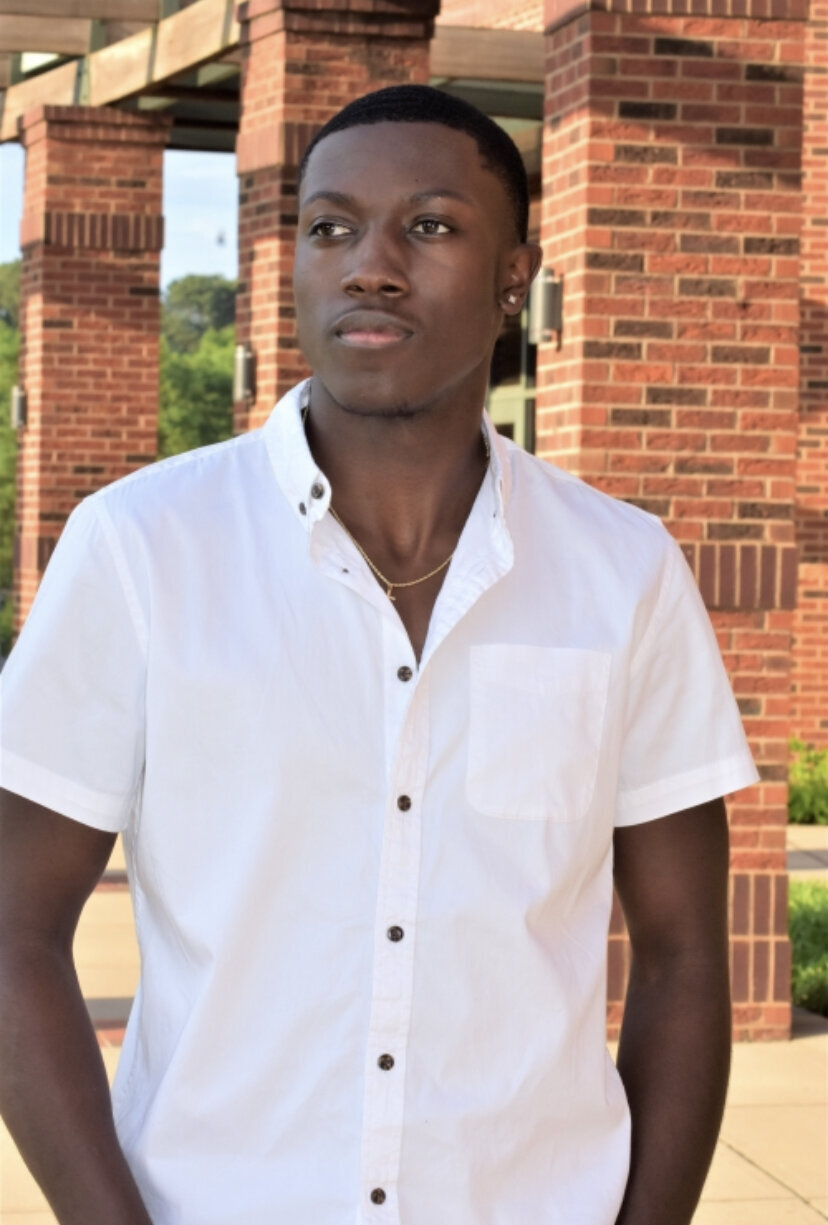 a senior dressed in a white button up shirt posing outside of the school for his graduation photos photographed by Millz Photography in Greenville, SC