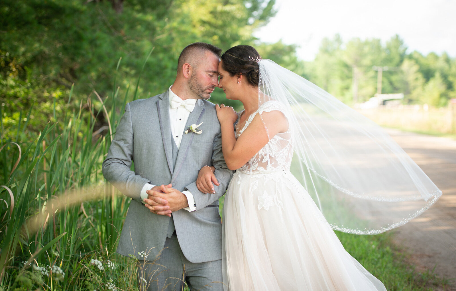 bride holds groom's shoulder while veil billows