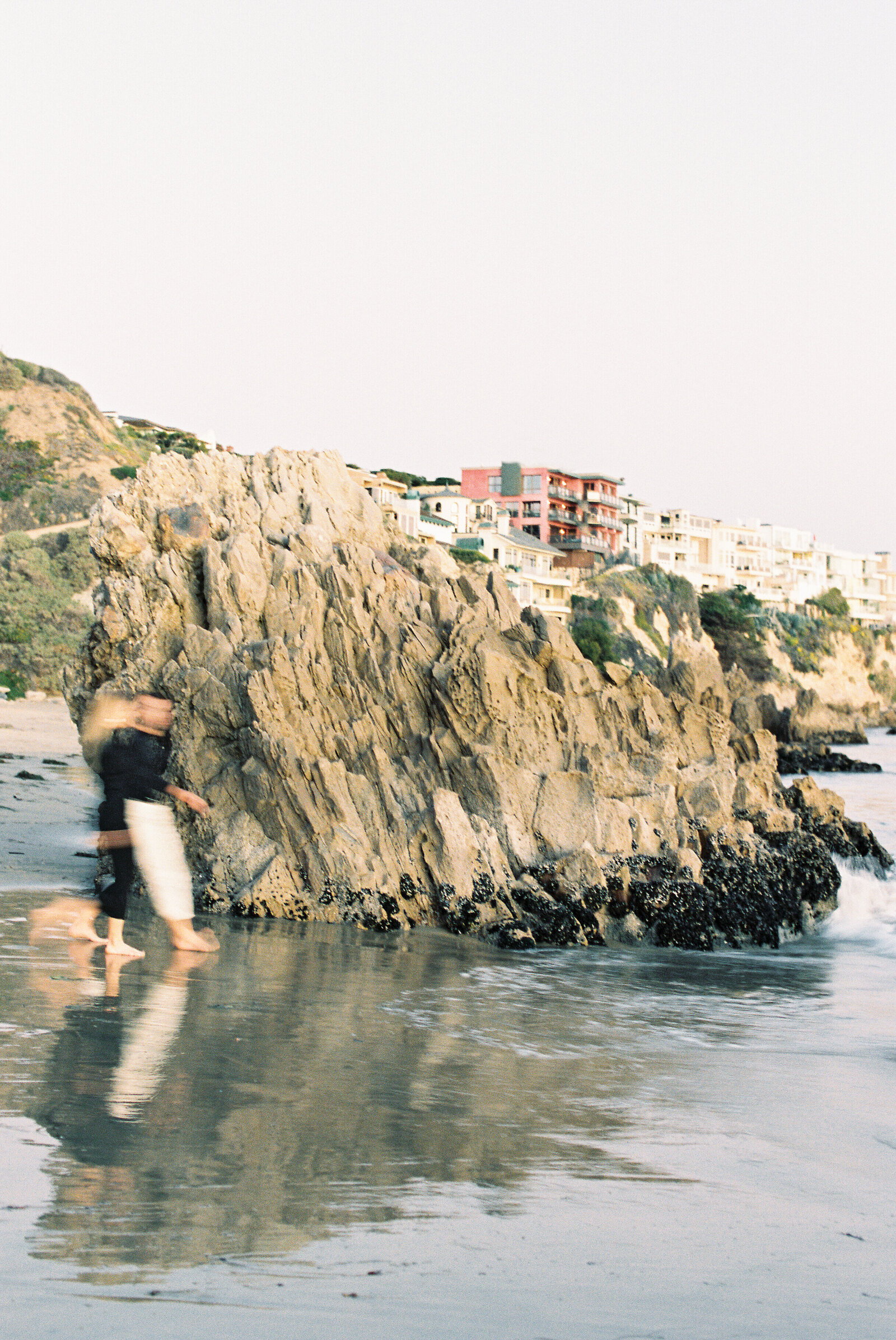 Blurred image of  a couple walking along the beach in front of a large rock.