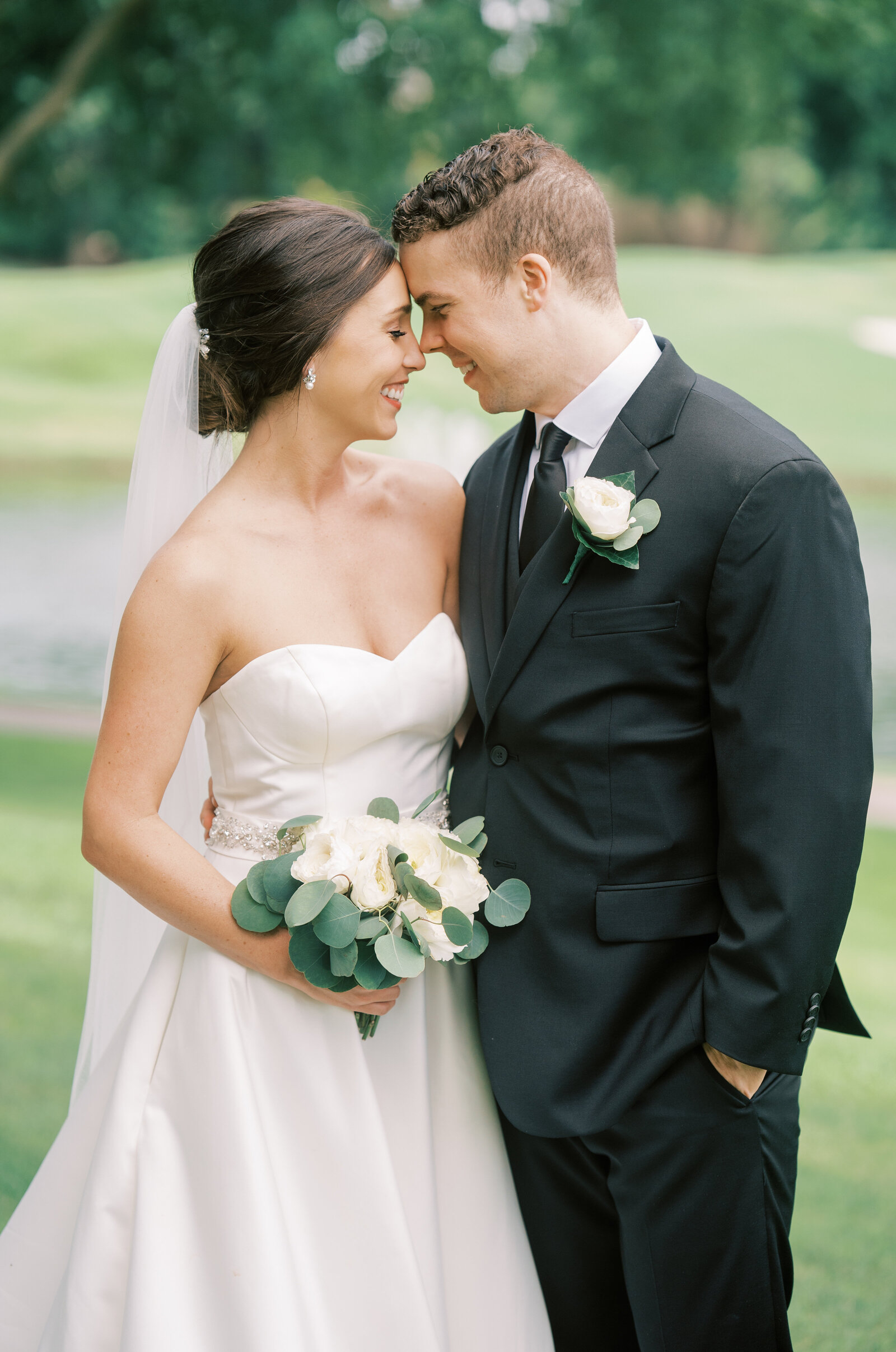 Portrait of bride and groom in a white wedding gown and black tuxedo on a green field.