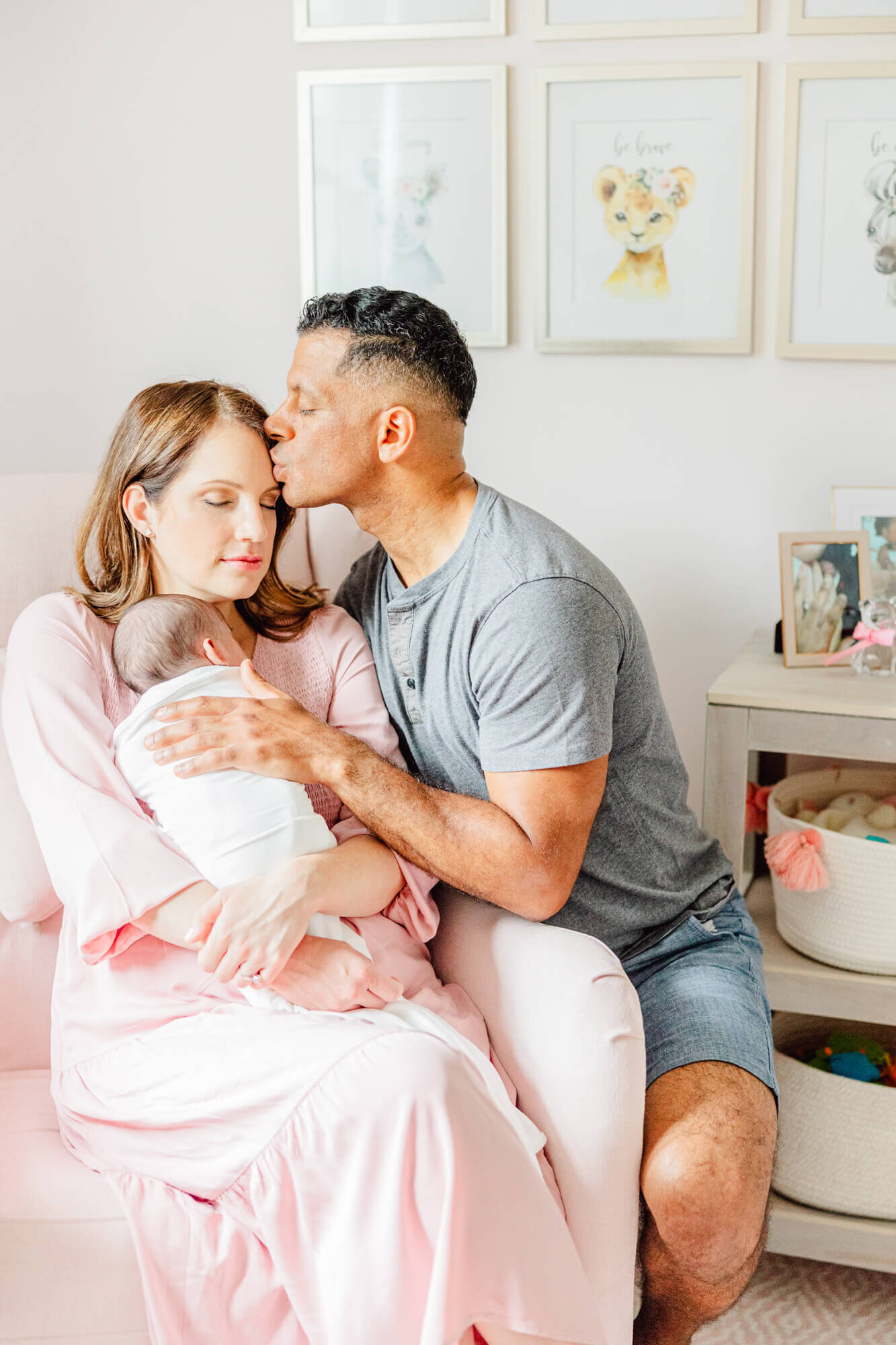 Dad kisses mom's forehead in the nursery while mom holds newborn