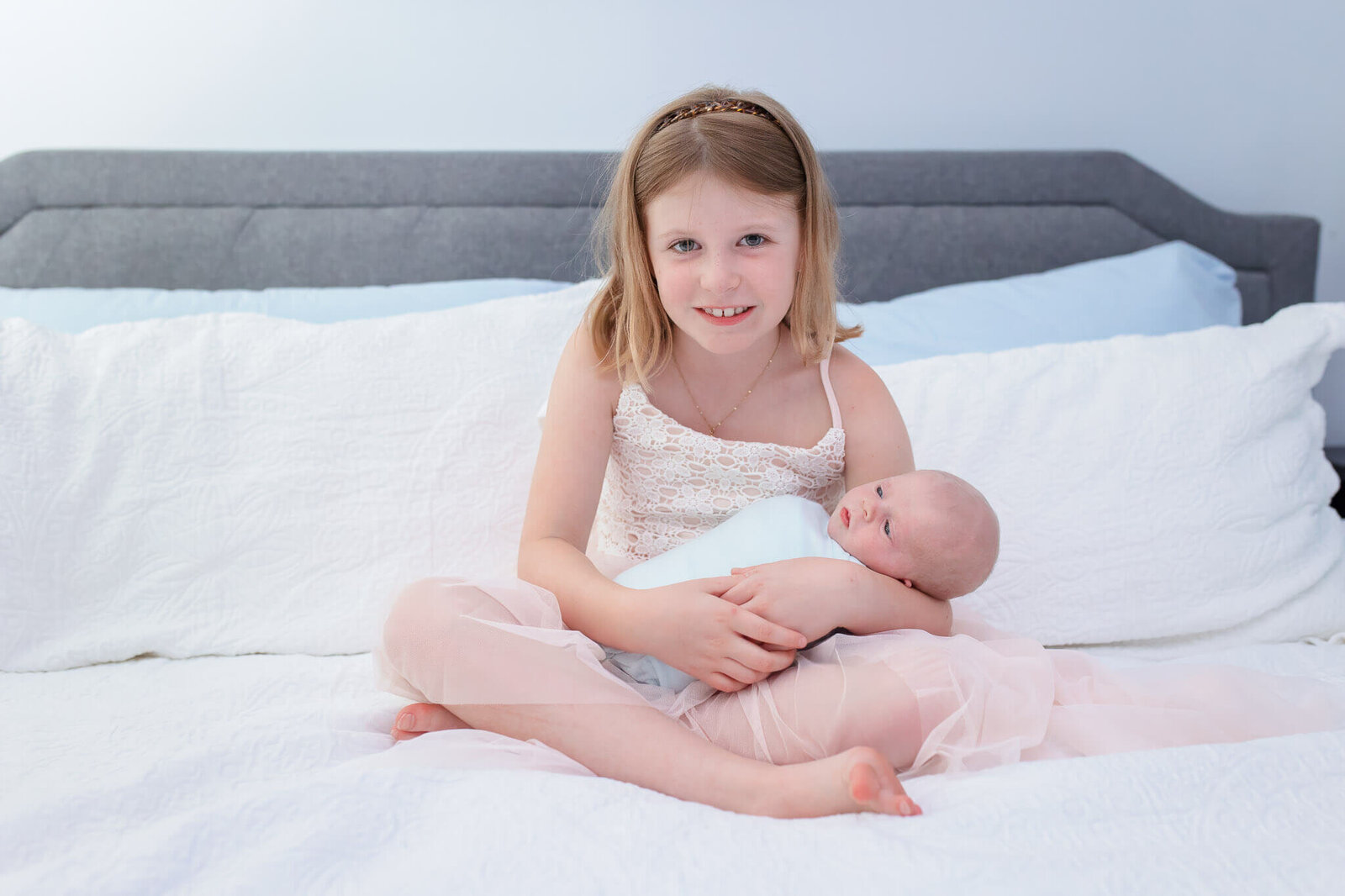 A little girl holding her newborn brother in bed.