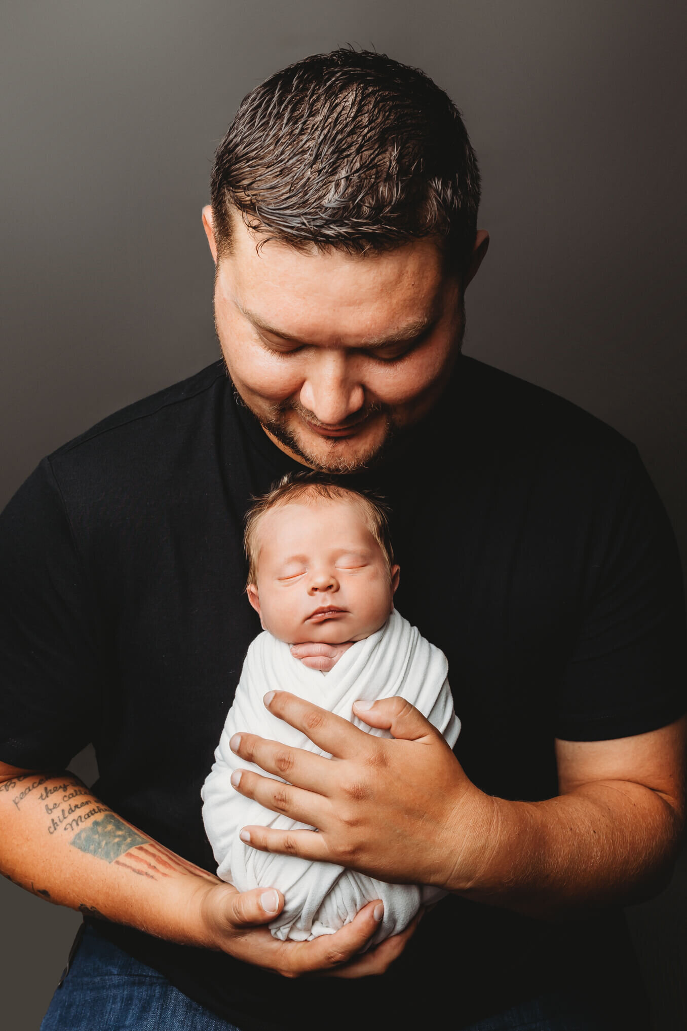 Dad in a black shirt holding swaddled newborn baby