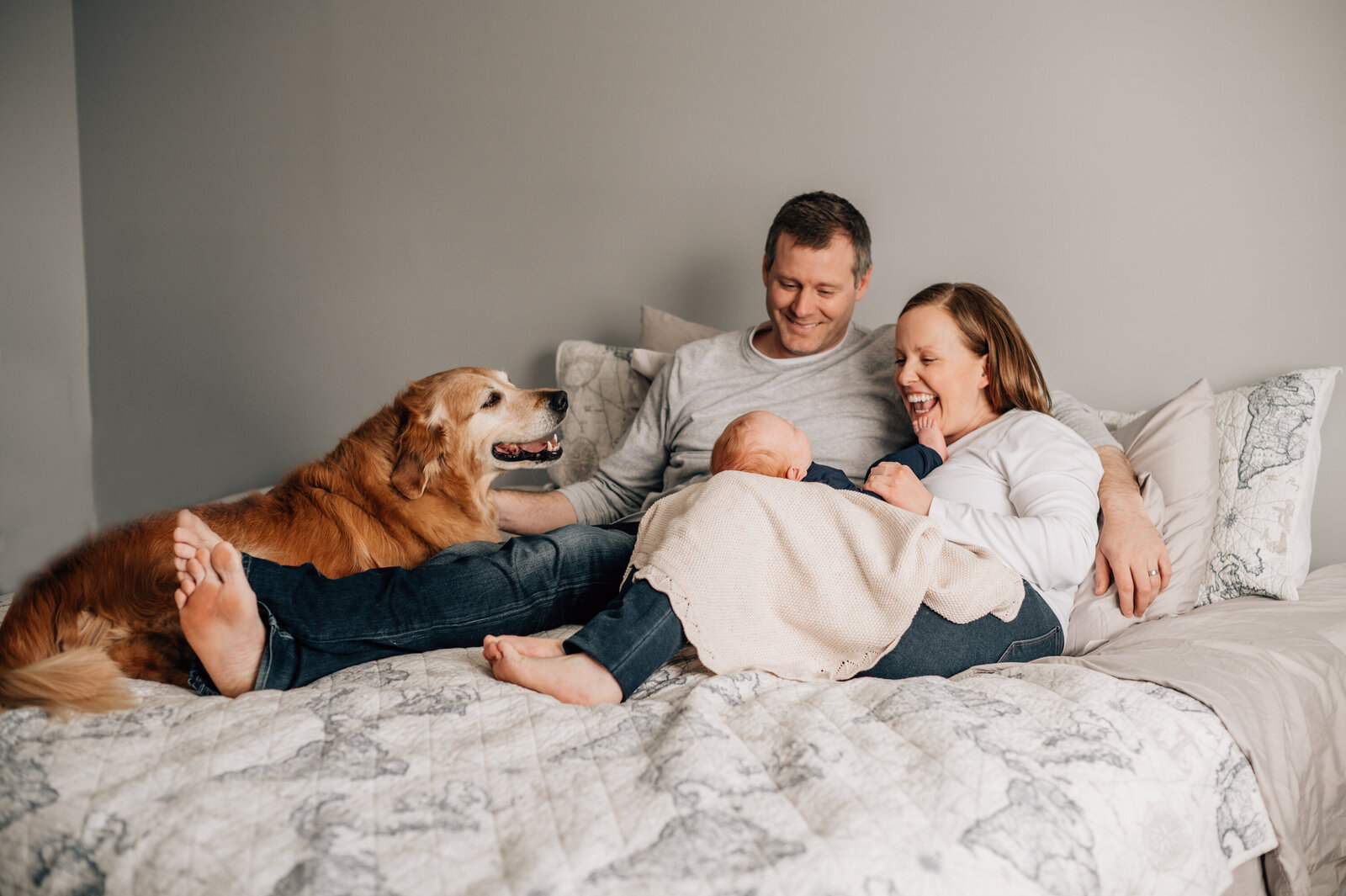 Mom, Dad and dog looking at their newborn baby lying on their bed.