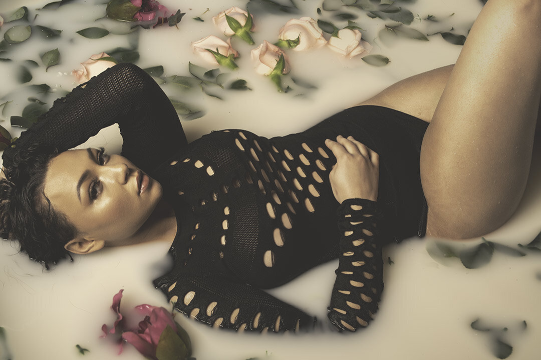 A gorgeous boudoir photo of a woman lying in a  steamy milk bath surrounded by roses.