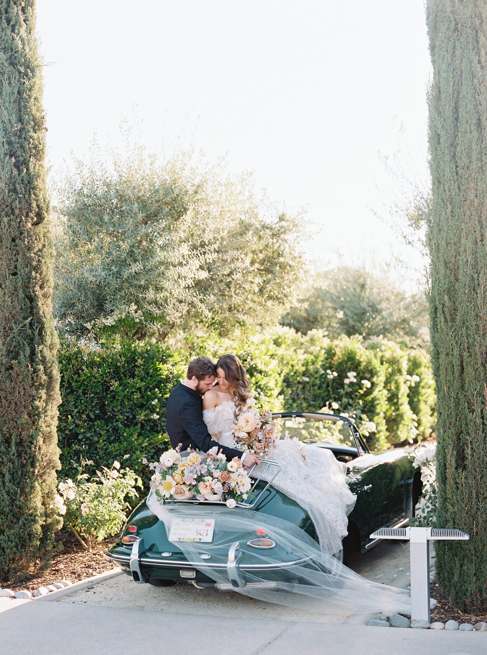 bride and groom sitting on a vintage dark green car