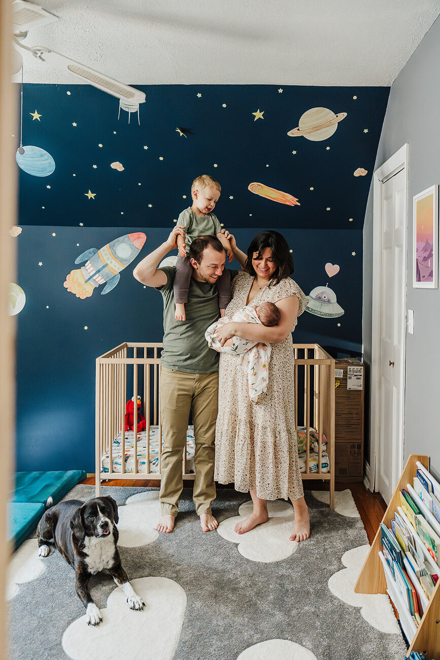 parents stand with new baby and toddler brother in space themed nursery
