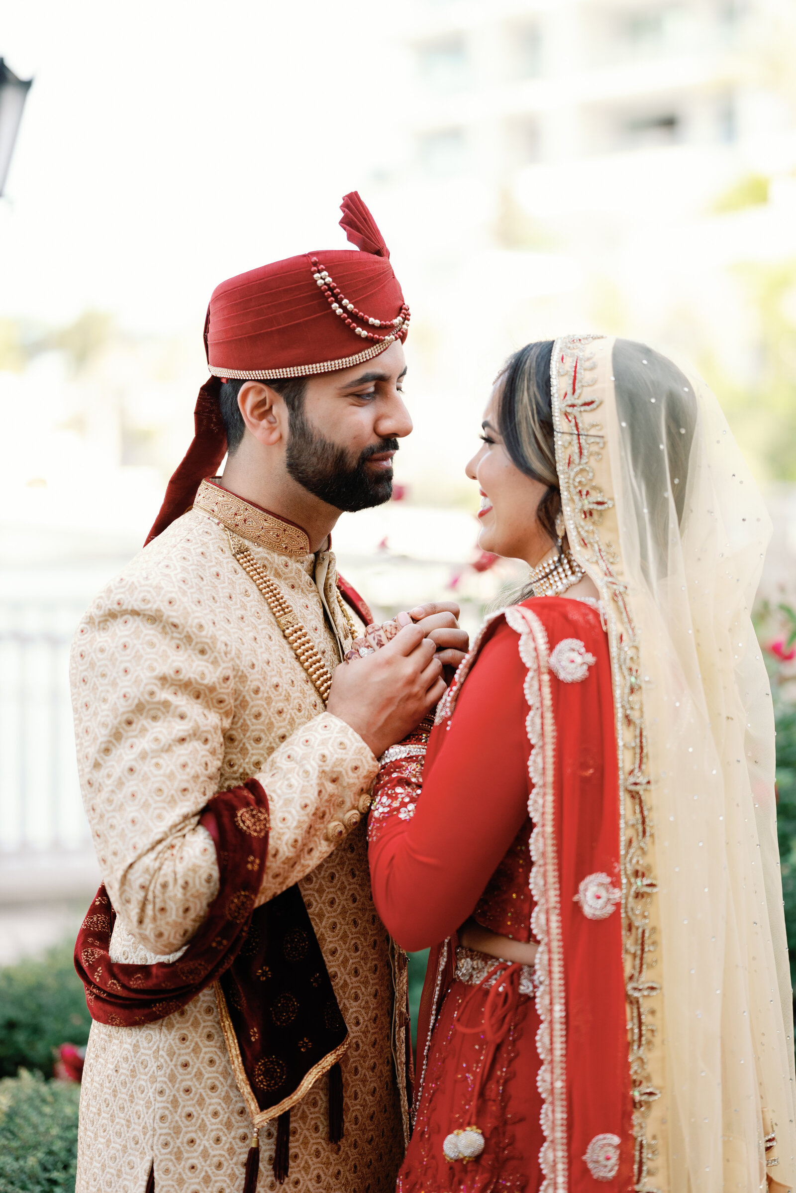 Indian wedding couple holding hands chest high while looking at each other and smiling right before they share a kiss