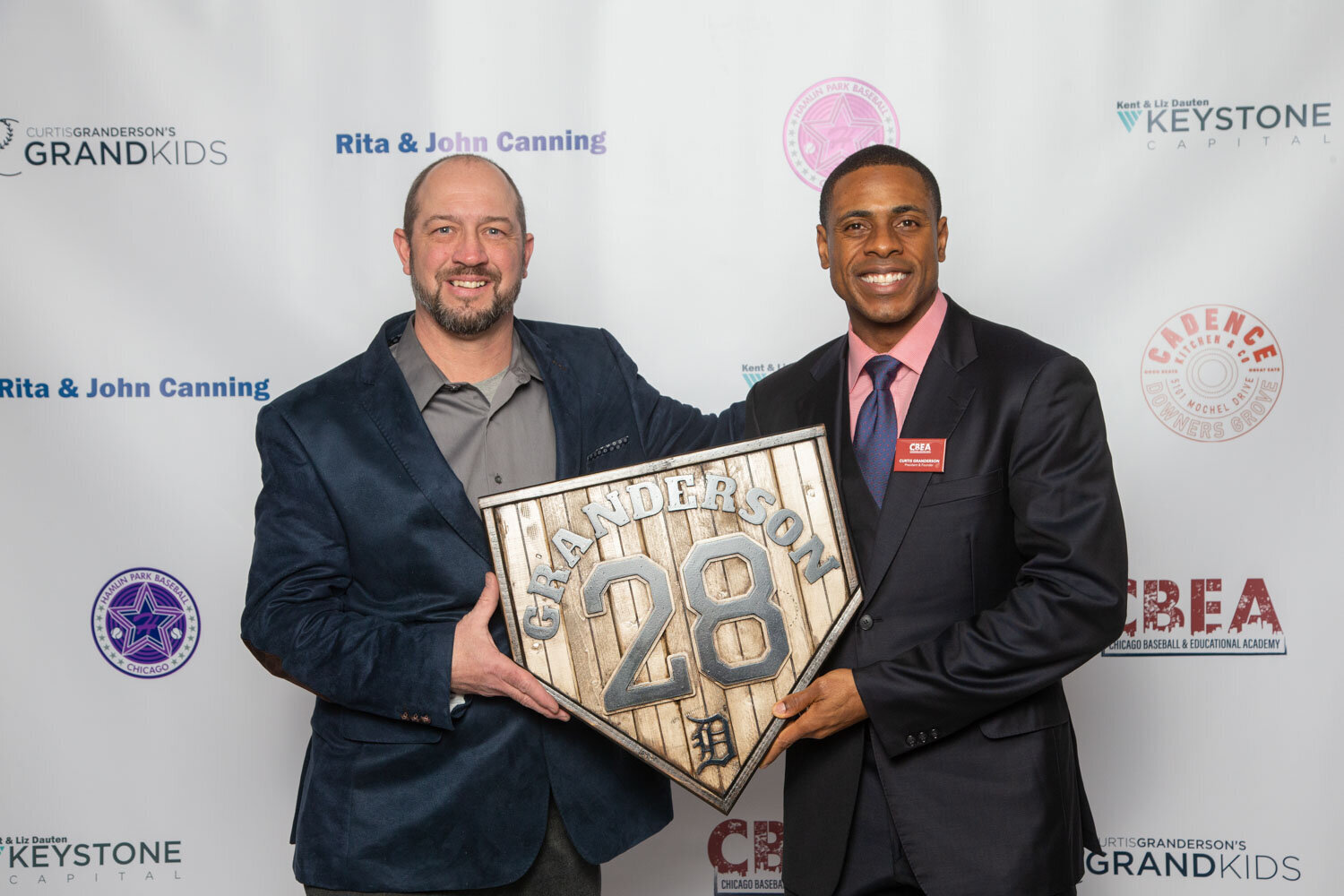 Two men holding a Granderson 28 sign at a photo backdrop