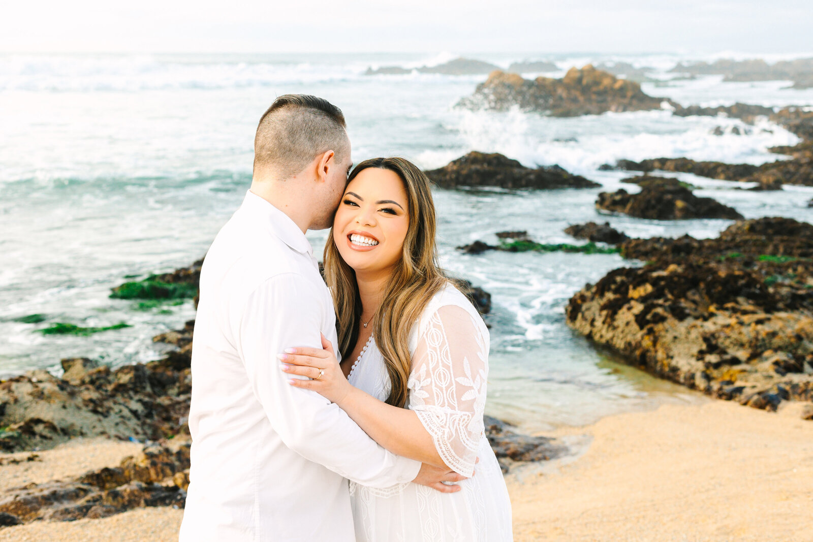An engaged man and woman take photos on the beach in Pacific Grove, Monterey, California near Big Sur.