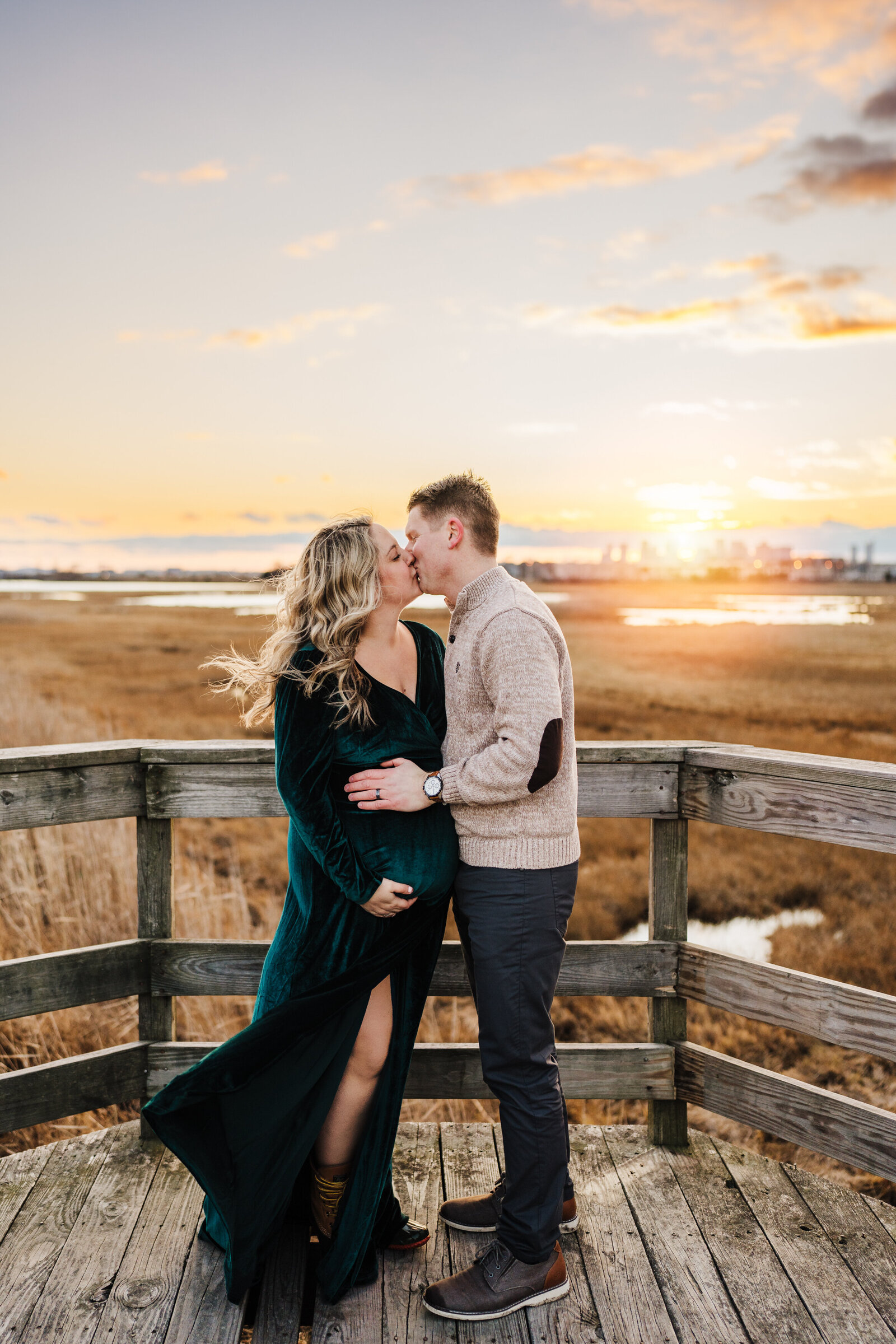 pregnant couple kisses by marsh at sunset