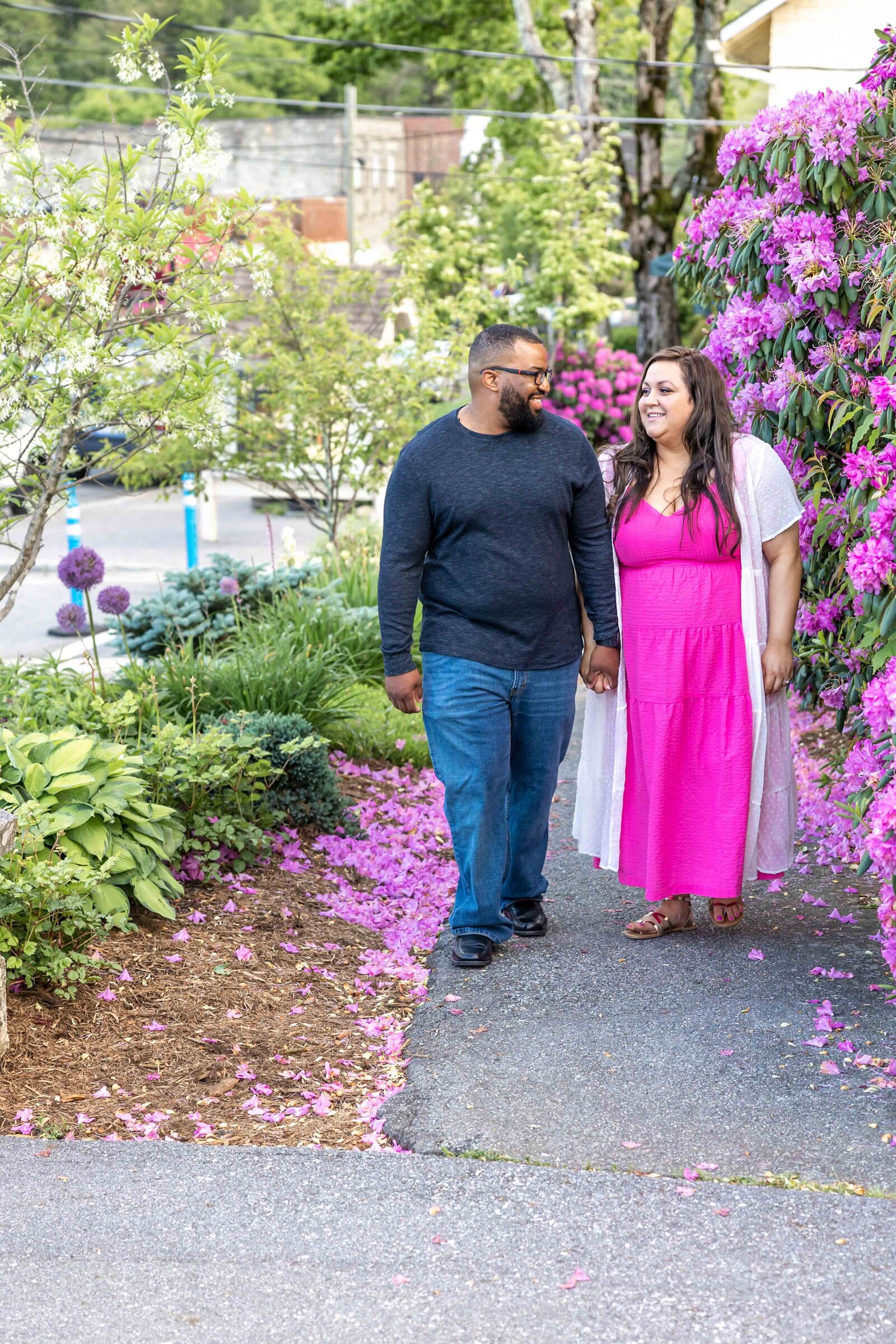 A joyful couple strolling down a flower-lined path in Boone, NC, surrounded by vibrant blooms and greenery. This image reflects the charm of artistic wedding photography, perfect for brides looking for affordable wedding photography in Wilmington.