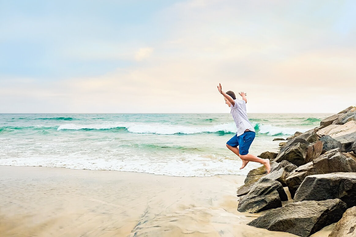 boy jumping from rocks at the beach in San Diego