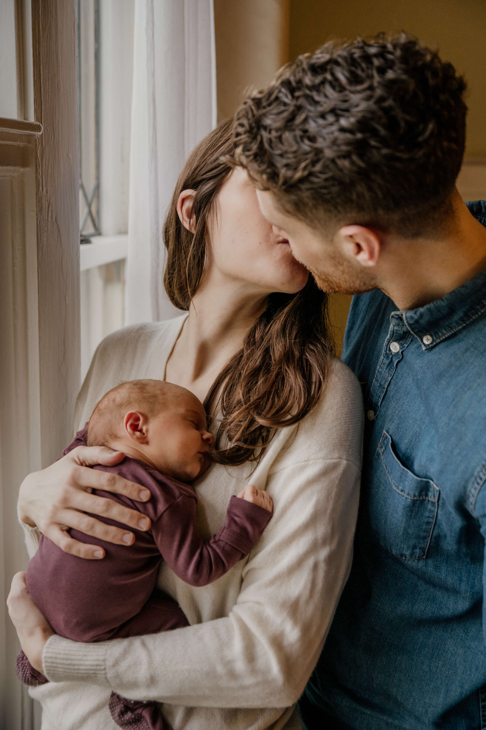 Couple kissing while holding baby.