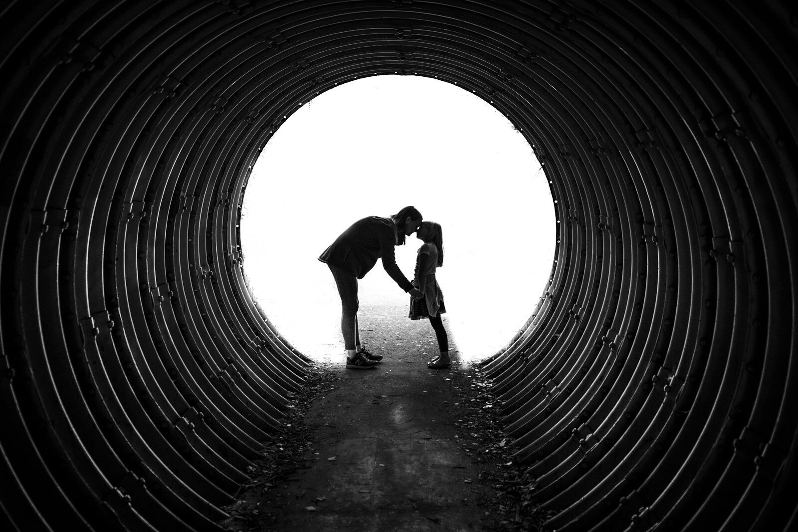 mom bending down to touch noses with daughter at the end of a park tunnel