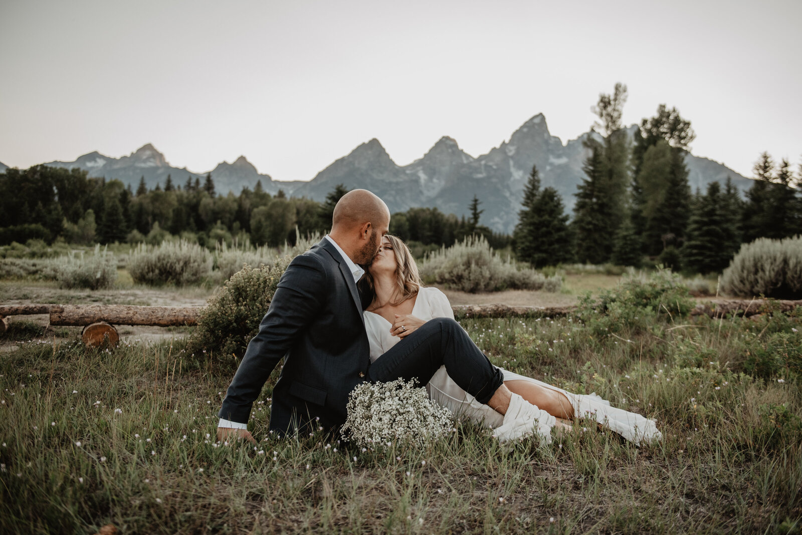 jackson hole photographers captures bride and groom sitting close in a meadow in the grand tetons for summer wedding
