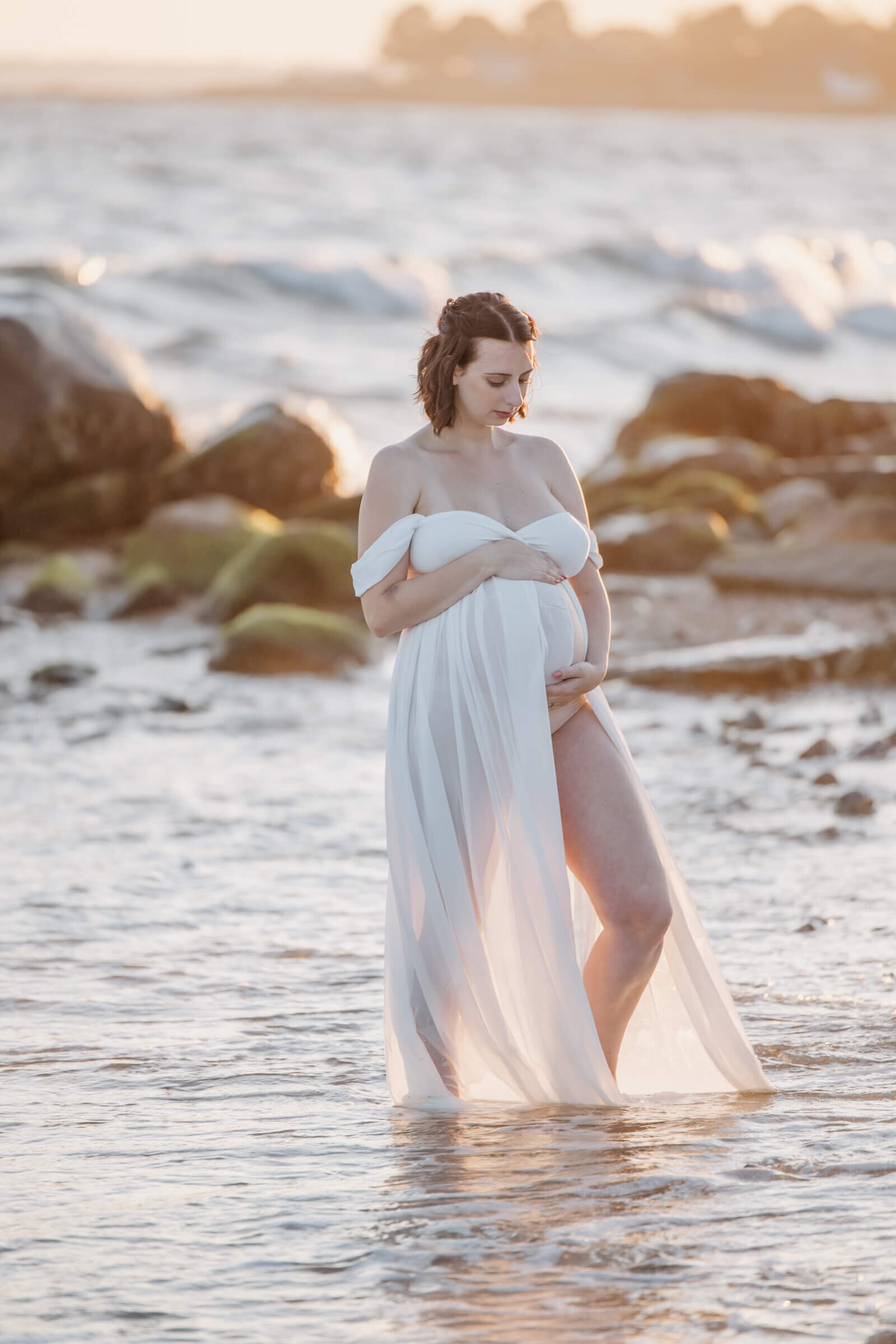 Pregnant woman in open dress at sunset in shallow water